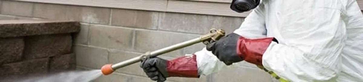 Pest control technician applying exterior insect treatment along a home foundation in Newark, NJ