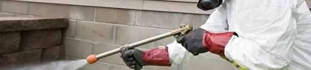 Pest control technician applying exterior insect treatment along a home foundation in Newark, NJ