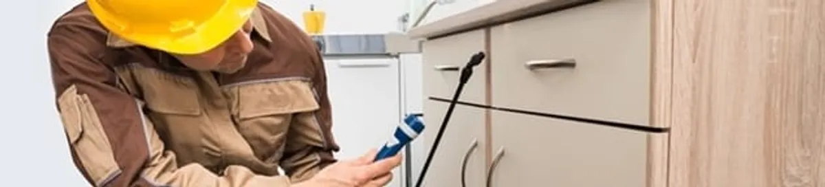 Roach exterminator applying treatment under kitchen cabinets in Newark, NJ