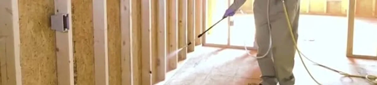 Termite treatment technician applying spray along framing and unfinished walls in Newark, NJ