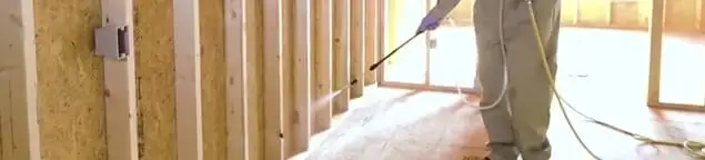 Termite treatment technician applying spray along framing and unfinished walls in Newark, NJ